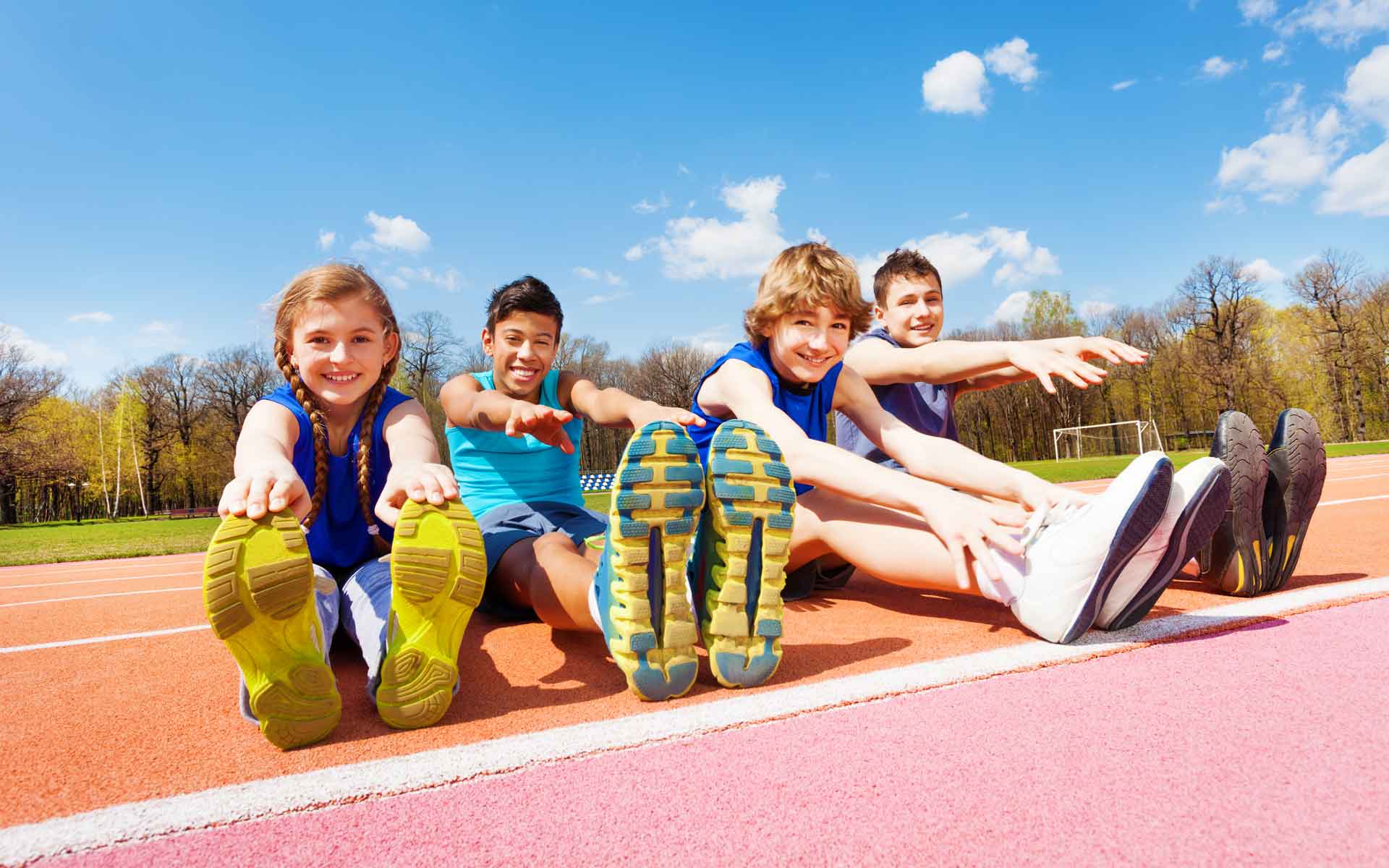 Niños sonrientes sentados en pista de atletismo listos para actividad